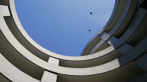 Low angle view of a parking building against blue sky with flying birds 