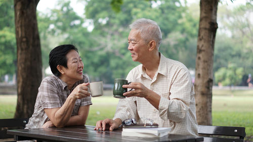 Smiling couple having drink while sitting in park