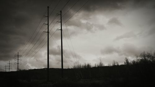 Low angle view of electricity pylon on field against cloudy sky