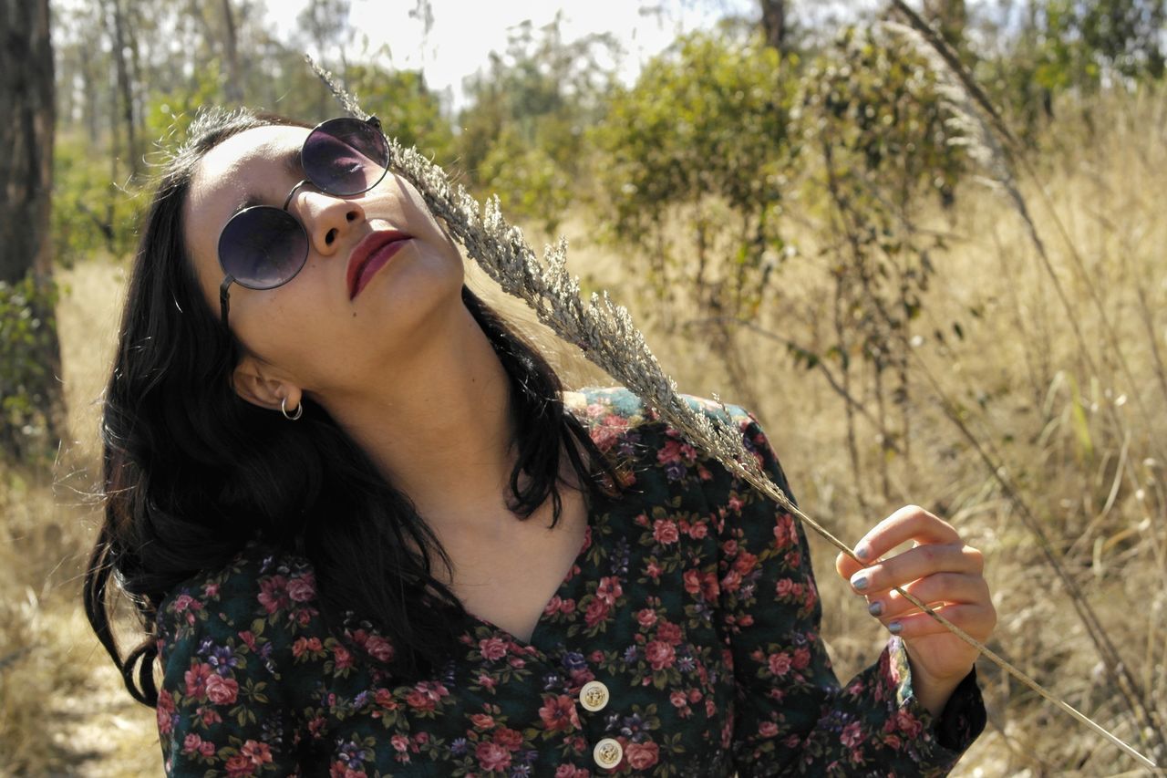 one person, young adult, lifestyles, leisure activity, real people, plant, young women, nature, focus on foreground, adult, portrait, day, holding, women, tree, casual clothing, sunglasses, glasses, hairstyle, hair, outdoors, beautiful woman, contemplation