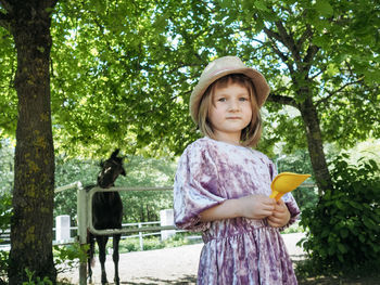 Portrait of small girl wearing lilac dress and summer hat and horse