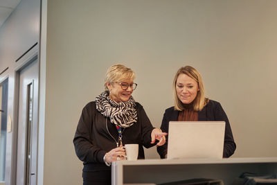 Portrait of smiling young woman using mobile phone while standing in office