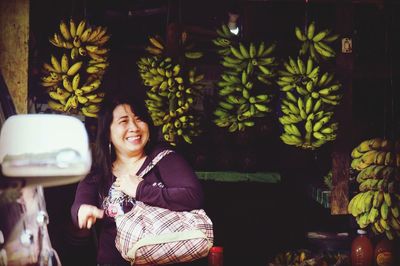 Smiling woman standing by bananas for sale at market