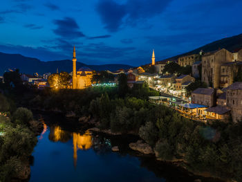 Illuminated buildings by river against sky at night