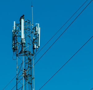 Men on communications tower against clear blue sky