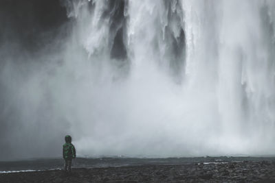 Silhouette child standing against waterfall