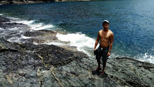 High angle view of shirtless man standing at rocky shore