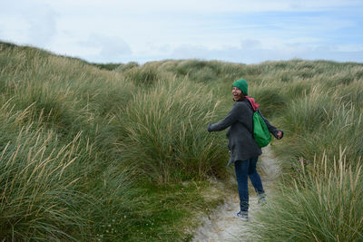 Rear view of woman walking on field against sky