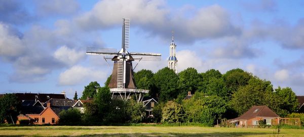 Traditional windmill by trees and house against sky