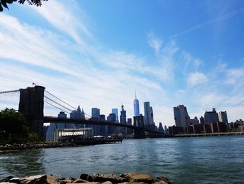 Brooklyn bridge over east river by city skyline against sky