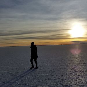 Silhouette woman walking at beach against sky during sunset