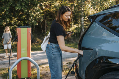 Side view of woman removing electric plug after charging car at station