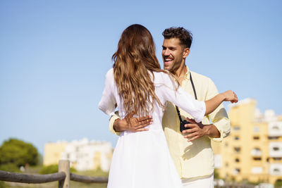Young couple embracing while standing against clear sky