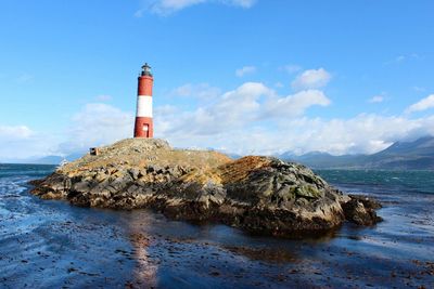 Lighthouse on rock by sea against sky