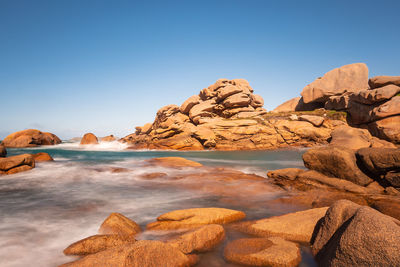 Scenic view of rocks in sea against clear blue sky