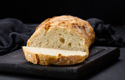 Baked whole oval bread made from white wheat flour on a black table, fresh pastries