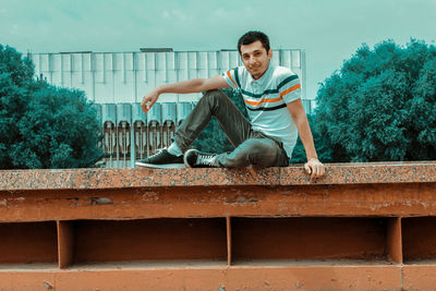 Portrait of young man sitting against wall