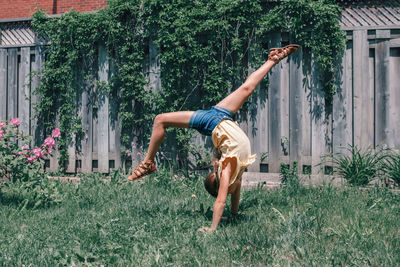 Girl balancing on handstand at yard against fence