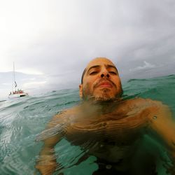 Shirtless man swimming in sea against cloudy sky