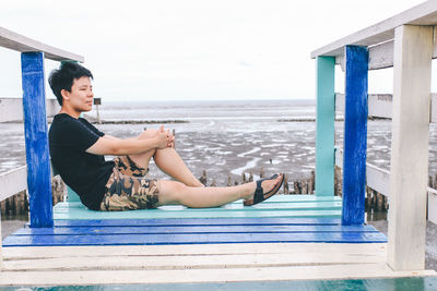 Side view of woman sitting on swimming pool against sea