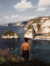 Rear view of shirtless man looking at sea against sky