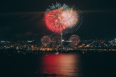 Firework display over illuminated city against sky at night