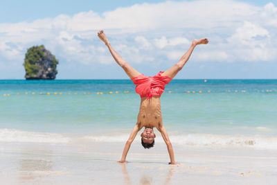 Full length of shirtless boy practicing handstand at beach