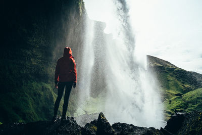 Rear view of man looking at waterfall against sky
