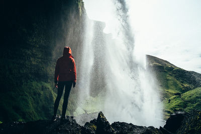 Rear view of man looking at waterfall against sky