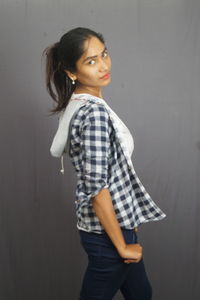 Young woman looking away while standing against wall