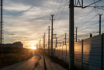 Electricity pylons against sky during sunset