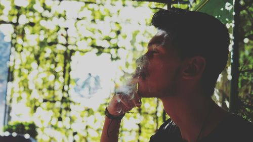 Close-up of young man smoking against tree