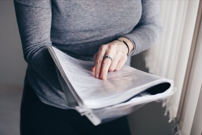 Midsection of businesswoman reading file while standing by window in office