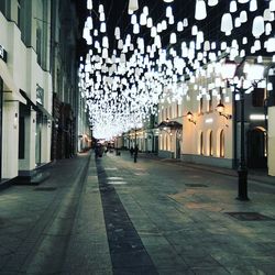 Illuminated street lights on footpath amidst buildings in city