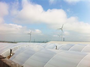 Polyethylene tunnel by wind turbine against sky