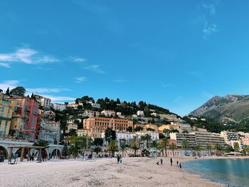 Scenic view of beach by buildings against blue sky