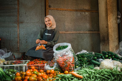 Portrait of young woman picking vegetables for sale at market stall
