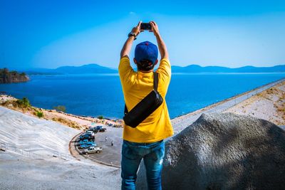 Rear view of man photographing on mobile phone against sky