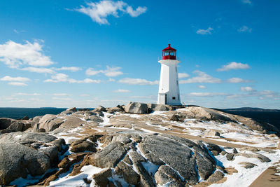 Lighthouse on beach by buildings against sky