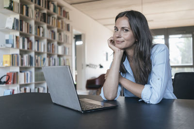 Portrait of smiling woman sitting at table with laptop