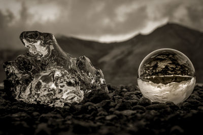 Close-up of crystal ball at beach against cloudy sky