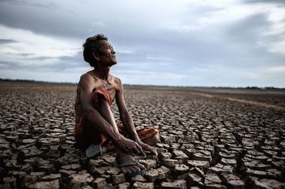 Young man sitting on land against sky
