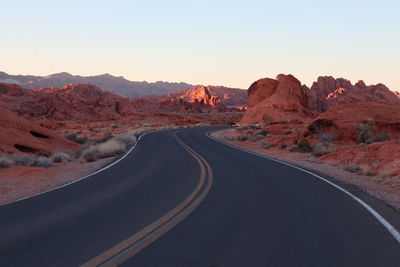 Road leading towards mountains against clear sky