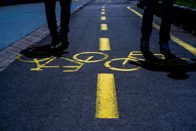 Low section of men standing on road with bicycle sign