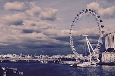 Ferris wheel by river against sky in city