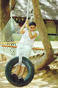 Portrait of happy girl on tire swing by hammock over field