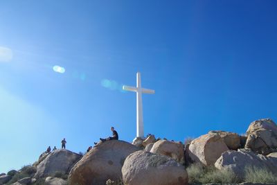 Low angle view of cross on rocks against clear blue sky