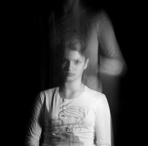 Close-up of young woman standing against black background