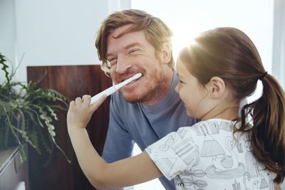 Daughter brushing her father’s teeth in bathroom