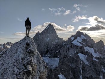 Rear view of man standing on snowcapped mountain against sky